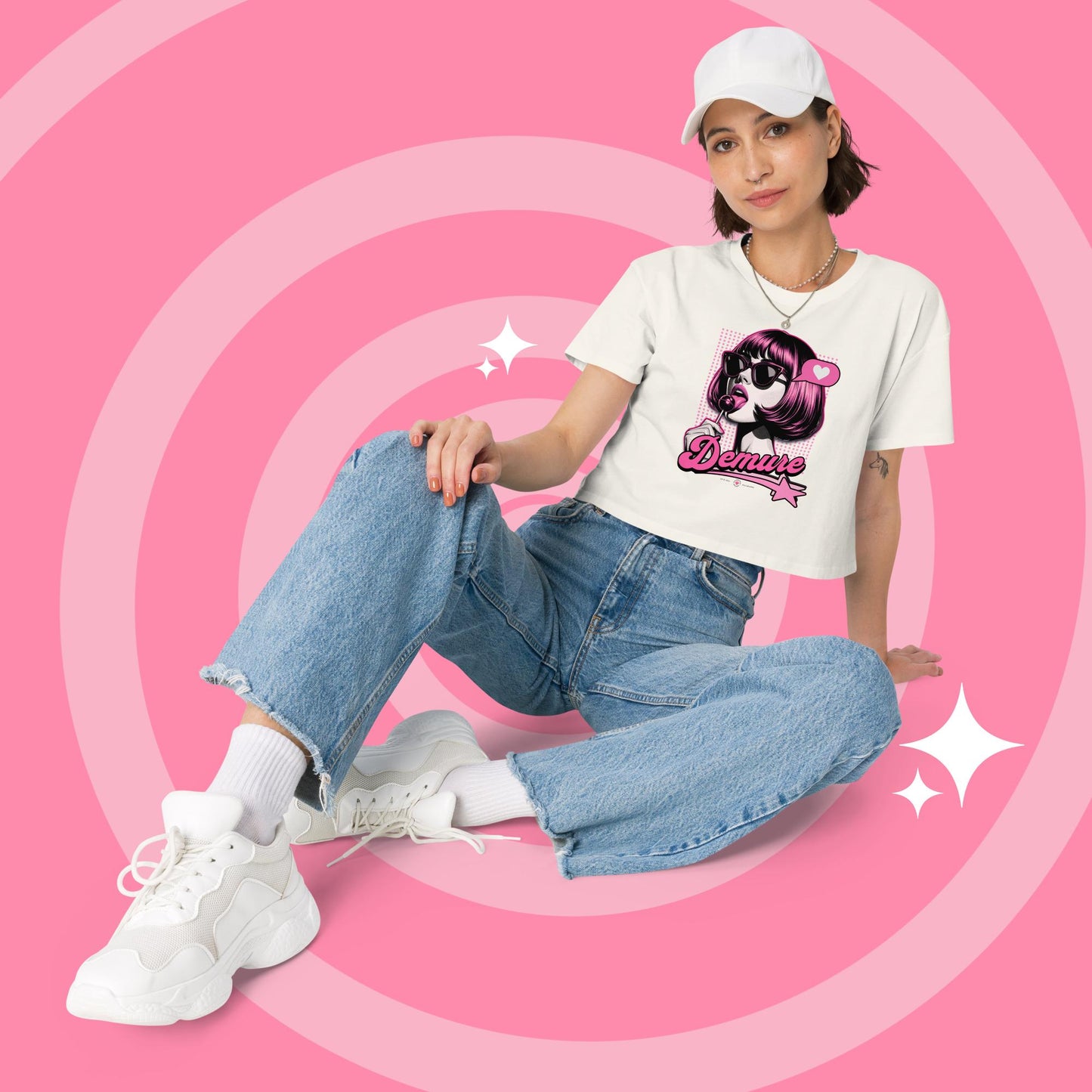 Woman wearing a ecru cropped graphic T-shirt and jeans sitting.