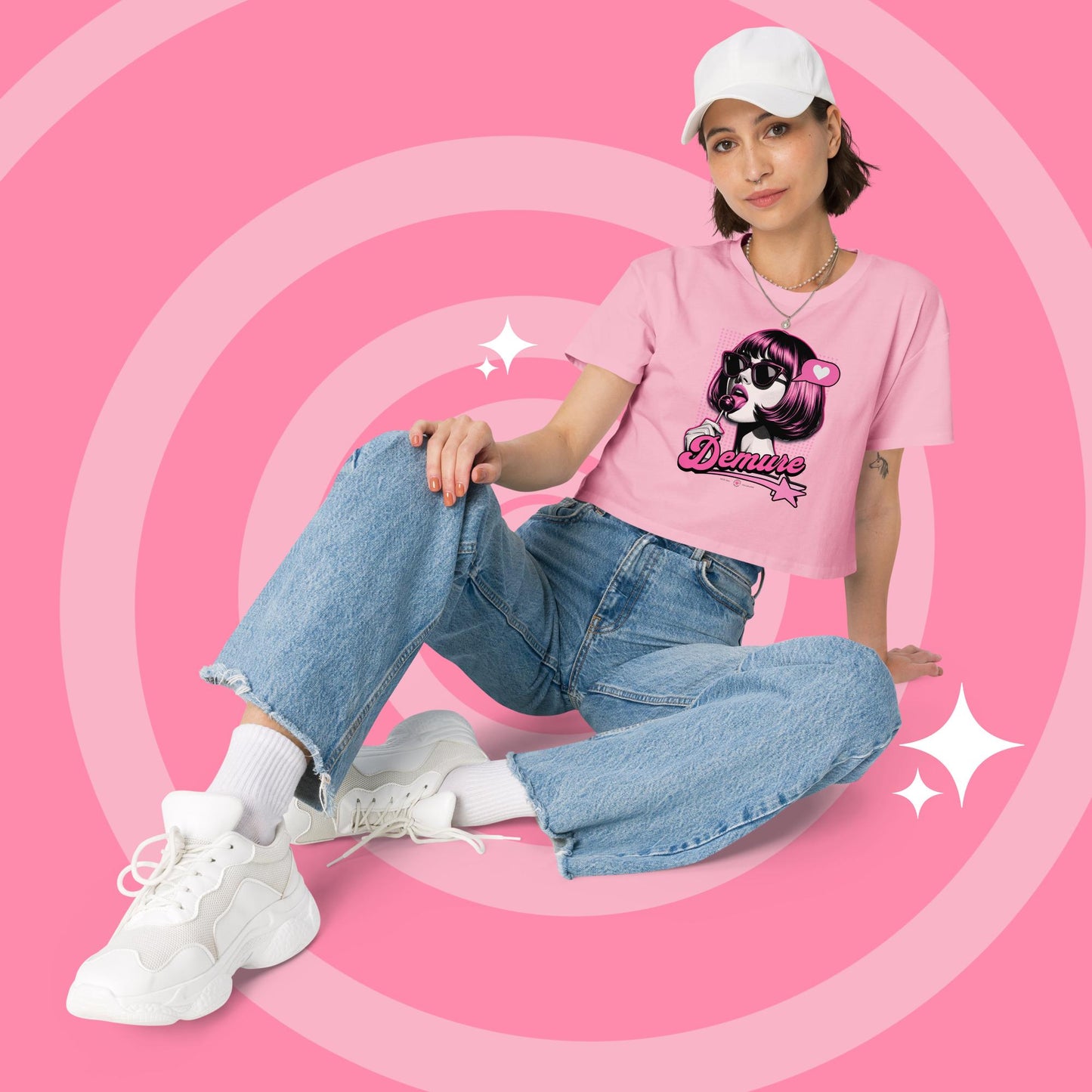 Woman wearing a pink cropped graphic T-shirt and jeans sitting.