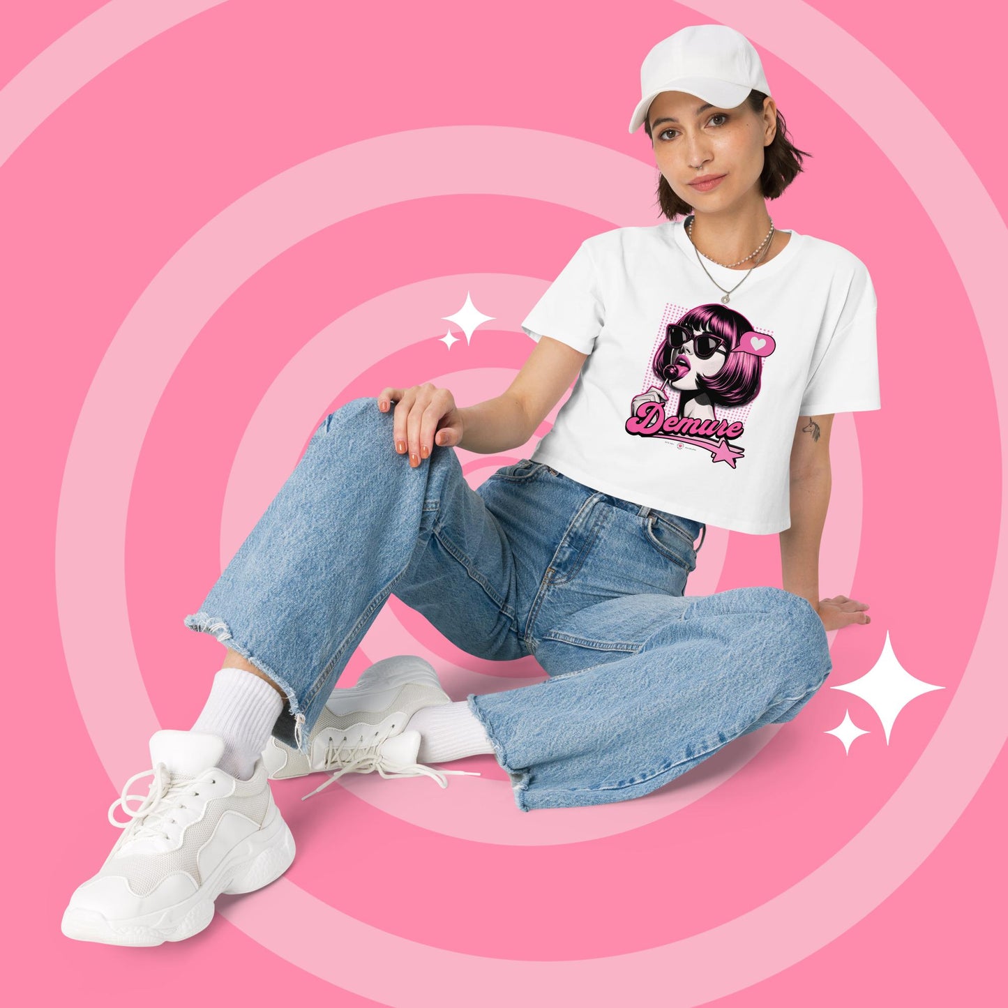 Woman wearing a white cropped graphic T-shirt and jeans sitting.